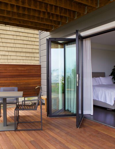 Modern bedroom opening onto a wooden deck with outdoor seating.