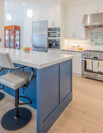 Modern kitchen interior with blue island and bar stools, stainless steel appliances, and white cabinetry.