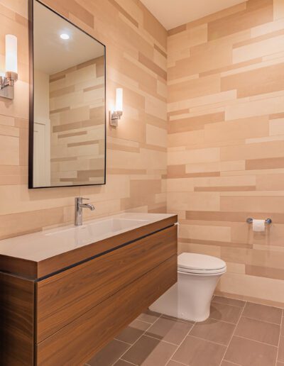 Modern bathroom with beige tiled walls, wooden vanity, and wall-mounted mirror.