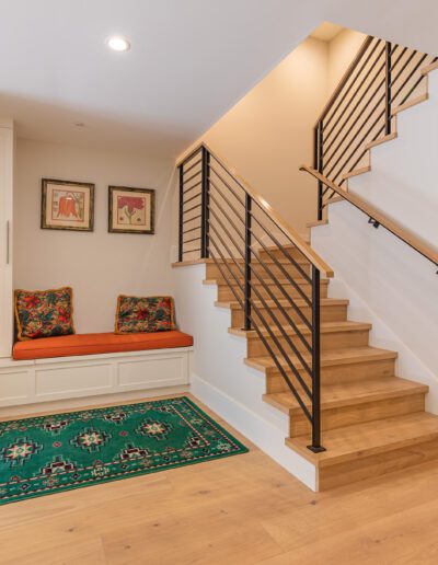 Modern home interior with a staircase, built-in seating area with colorful cushions, and a green patterned rug.