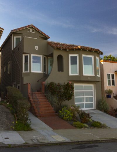 A residential building on a sloped street with a set of stairs leading up to the entrance.