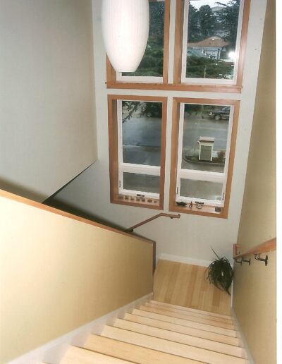 Wooden staircase leading down to a landing with a large window offering a view of the outside street.