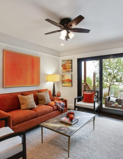 A modern living room with a red sofa, contemporary art pieces, and a glass coffee table, opening onto a balcony.
