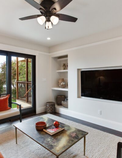 Modern living room with a mounted television, ceiling fan, and sliding doors leading to an outdoor area.