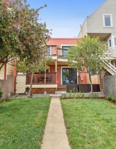A landscaped backyard leading to a modern house with a balcony and sliding glass doors.