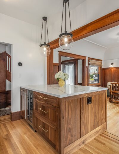Open kitchen and dining area with wooden cabinetry, a central island, hardwood floors, and traditional style wooden beams along the ceiling.